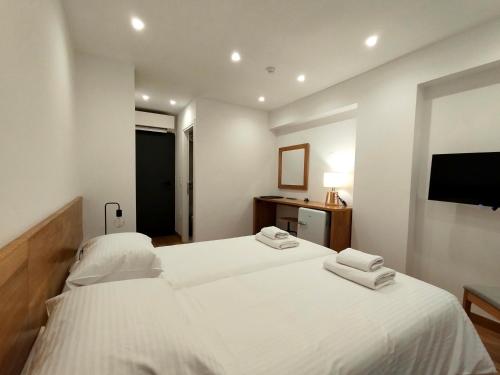 a white bedroom with two beds and a television at Marelia Urban in Thessaloniki