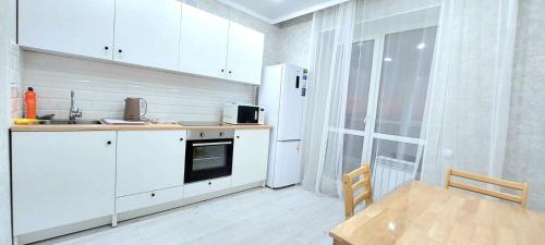 een keuken met witte kasten, een tafel en een koelkast bij Аэропорт 10 минут жк Будапешт163 in Astana