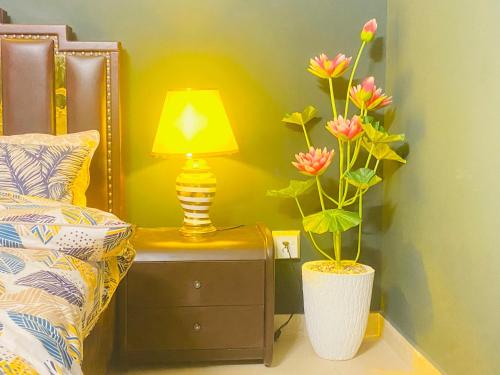 a lamp on a nightstand next to a bed with flowers at Three Bed Premium Apartment in Islamabad