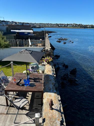a table with an umbrella on a dock in the water at Splash Cottage beach house with Sea lapping Garden in Bangor