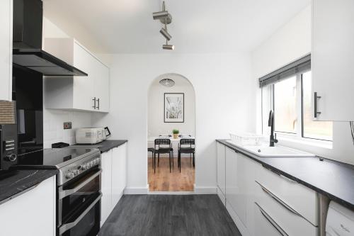 a white kitchen with black countertops and a table at Amazing 3Bed 2Bath House with Garden, Parking, WiFi Near Stevenage Train Station in Aston End