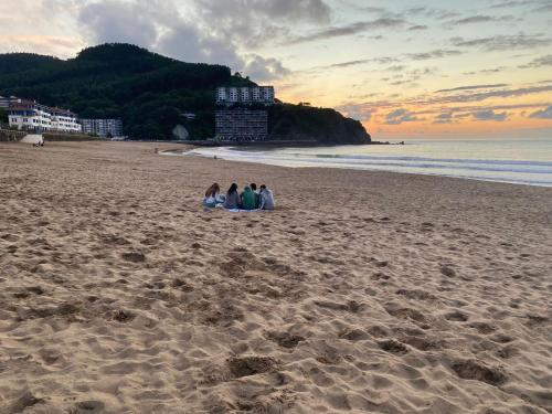 three people sitting on the beach at sunset at Bakio, magnificas vistas a la mar in Bakio