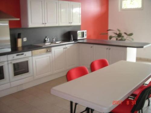 une cuisine avec des placards blancs et une table avec des chaises rouges dans l'établissement Les Epinettes, à Cagny