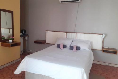 a bedroom with a white bed with two pink pillows at Ochsenwagen Pension Hotel in Rehoboth