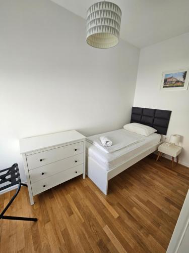 a white bedroom with a bed and a dresser at HOME APARTMANI I SOBE in Osijek