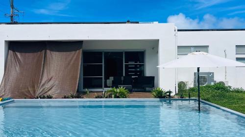 a swimming pool with an umbrella next to a house at UmiOto ウミオト 夫婦 カップル 女性一人旅に大人気のナイトプール付き ゲストハウス 宮古島 in Miyako-jima