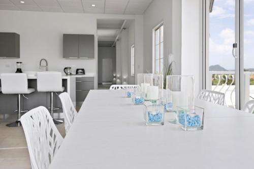 a white kitchen with a long white table and chairs at Bocobay Penthouse 4BR 4BA with Rooftop Pool in Oranjestad