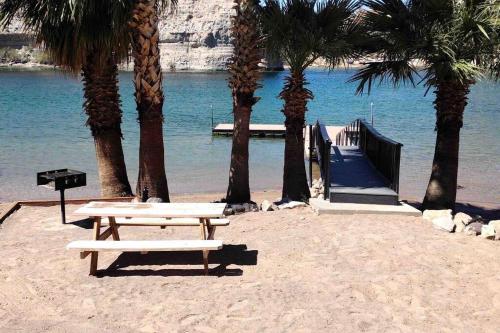 a picnic table on a beach with palm trees and a dock at Love nest in Bullhead City