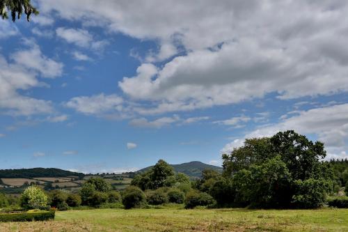 a field with trees and a blue sky with clouds at Llangattock Park House in Crickhowell