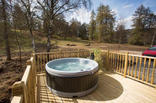 a hot tub on a wooden deck with a fence at Bluebell Lodge - Sleeps 4 Hot Tub Loch & Woodland in Strathpeffer