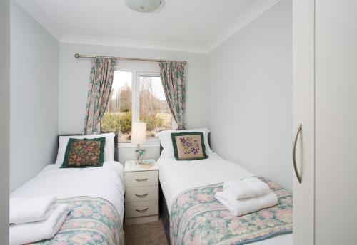 two twin beds in a room with a window at Bluebell Lodge - Sleeps 4 Hot Tub Loch & Woodland in Strathpeffer