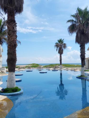 a pool with palm trees in front of the ocean at HOTEL CARASOL VILLAS & SUITES in Ciudad Madero