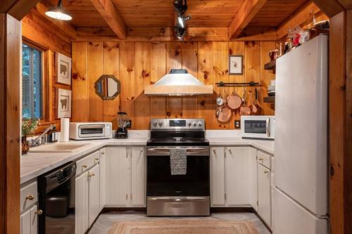 a kitchen with white cabinets and a black stove at Look to the Mountains: Gunstock Acres Log Cabin in Gilford