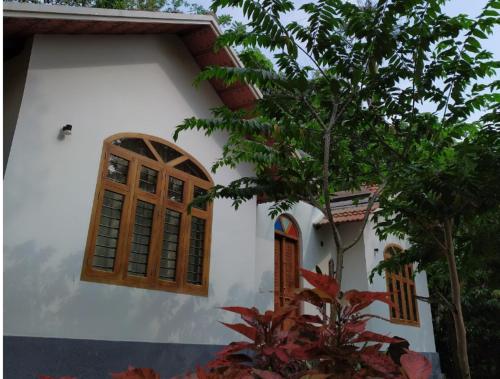 a white house with wooden windows and a tree at Serene Valley Resort Wayanad in Mananthavady