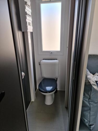 a bathroom with a toilet with a blue seat and a window at Mobil Home 6 Personnes Camping 5 étoiles Montalivet in Vendays-Montalivet