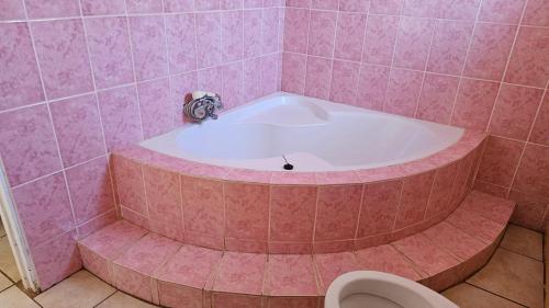 a pink bathroom with a tub and a toilet at Happy Stay Guest House Mafikeng in Mahikeng
