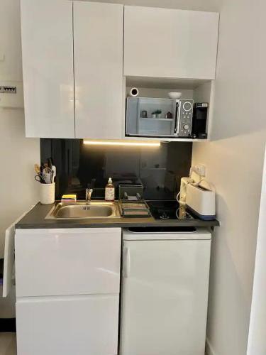 une cuisine blanche avec un évier et un micro-ondes dans l'établissement Bel appartement pour un séjour touristique, à Paris