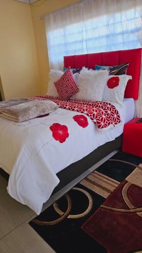 a bed with red and white blankets and pillows at Happy Stay Guest House Mafikeng in Mahikeng