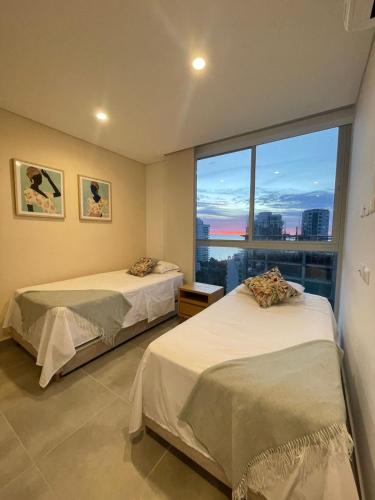 two beds in a room with a large window at Salguero Suites - Playa Salguero - By INMOBILIARIA VS in Santa Marta