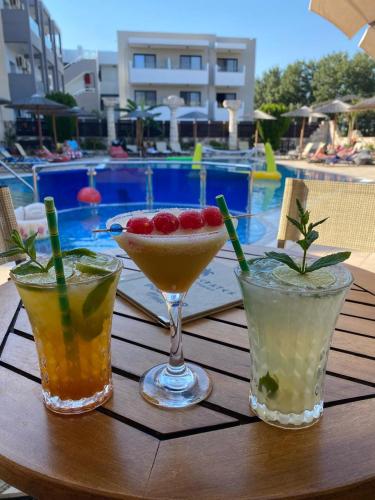 three cocktails sitting on a table near a swimming pool at Socrates Studios in Tigaki