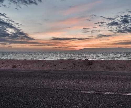 an empty road next to the ocean with a sunset at La hacienda Ras Sedr in Raʼs Matarma