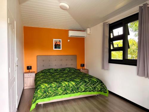 a bedroom with a green bed with an orange wall at TAHITI - Mango Lodge Hotu in Papara