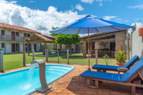 a swimming pool with a blue umbrella and chairs and a swimming pool at Pousada Trilha do Mar in Praia do Frances