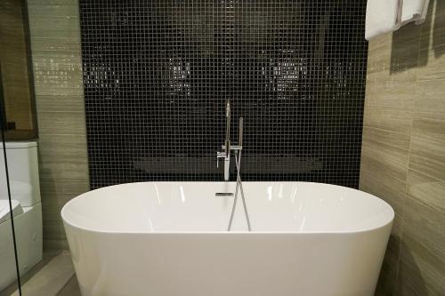 a white bath tub in a bathroom with black tiles at Swiss-Belhotel Airport Yogyakarta in Yogyakarta