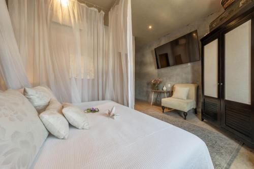 a bedroom with a white bed with a tv and a chair at Aruma Villa Boutique Isla Mujeres with beach club access included in Isla Mujeres