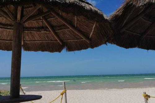 a beach with a straw umbrella and the ocean at Villa Nicte ha - Antalea in Telchac Puerto