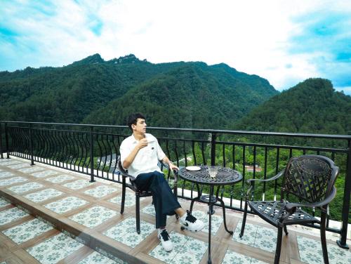 a man sitting at a table on a balcony with mountains at 张家界喜屋民宿 in Zhangjiajie