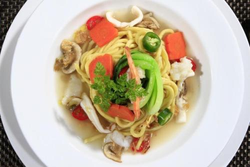 a bowl of soup with vegetables on a white plate at Mars City Hotel in Denpasar
