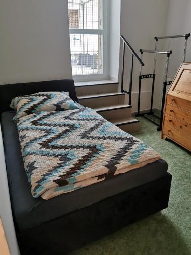 a bed with a blanket on it in a room with stairs at Dům na hradbách in Žatec