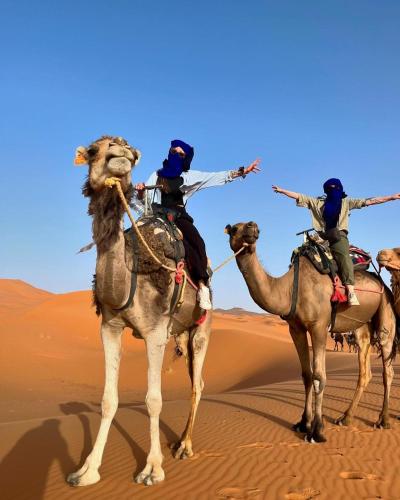 three people riding on the backs of camels in the desert at Merzouga Berbers Luxury Camp in Merzouga