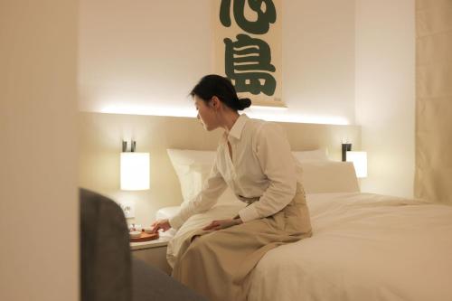 a woman sitting on a bed in a hotel room at Simdo Hotel&Spa Sillim by Aank in Seoul
