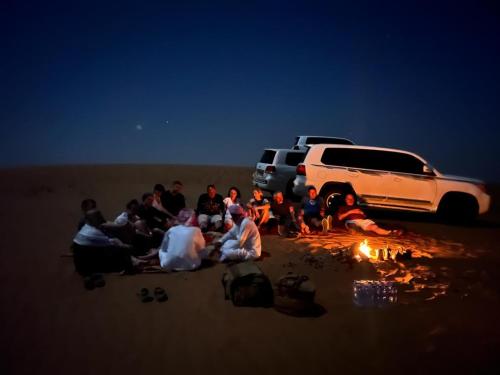 a group of people sitting around a fire in the desert at Al Salam Desert Camp Bidiya in Bidiyah