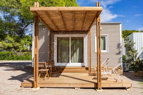 a cabin with a deck with chairs and a roof at HolaCamp Sitges Garrofer in Sitges
