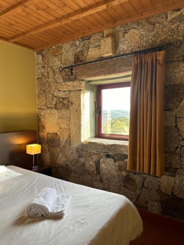 a bedroom with a stone wall with a bed and a window at Casa Entre-Palheiros e Casa do Canastro in Montalegre