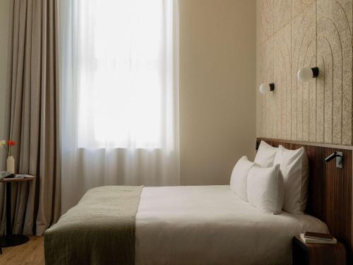 a bedroom with a bed with white sheets and a window at Hôtel Fort St Laurent Lyon - Handwritten Collection in Lyon
