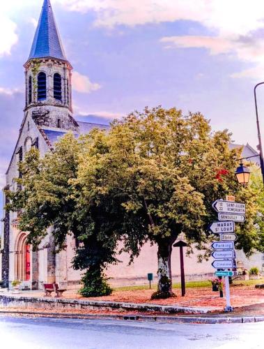 une église avec une tour, un arbre et des panneaux de rue dans l'établissement Auberge du chant du coq, à Anjouin
