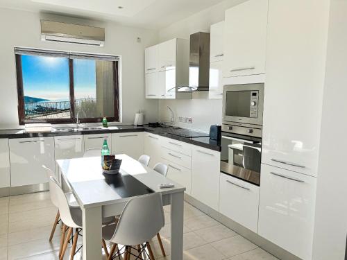 a kitchen with white cabinets and a table with chairs at Fort Chambray Holiday Villas & Apartments in Mġarr