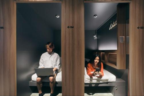 a man and a woman sitting on beds with a laptop at UNPLAN Fukuoka in Fukuoka