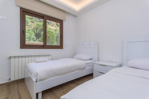 two beds in a white room with a window at Vantage - 2 BR Apt by The Valley in Kfardebian in ‘Ayn Barq