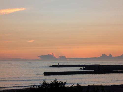 a sunset over the ocean with a pier at mahaloha house 新築ビーチフロント ペット同伴プラン有 ｍax8名 BBQ 海歩1分 アイランドキッチン 大型プロジェクタ 床暖房 オーシャンビューバス in Isumi