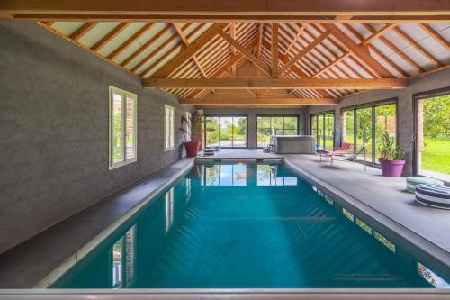 une piscine intérieure avec un toit en bois dans l'établissement La Baronnerie Normande - Piscine et jacuzzi, à Baromesnil