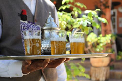 a man holding a tray with four glasses of beer at Domaine de la Roseraie Resort in Ouirgane