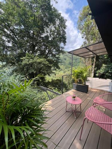 a wooden deck with pink chairs and a table at Entremonte Cabañas in La Vega