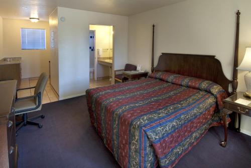 a hotel room with a bed and a desk and a chair at American Executive Inn Mesa in Mesa