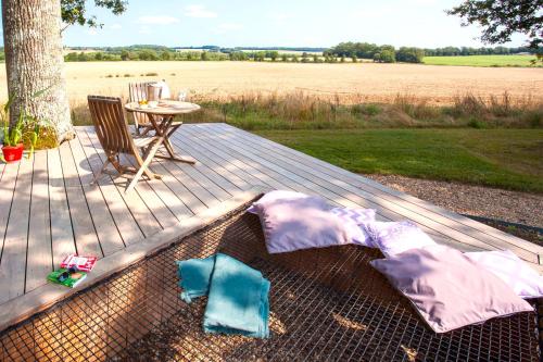 a deck with two pillows and a table and a field at Gîte La Parenthèse pour 2 avec SPA et SAUNA Privatif in Saint-Fargeau