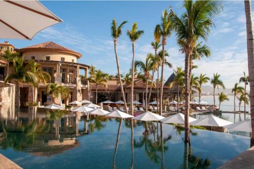 a pool at a resort with palm trees and umbrellas at 2 BD 5-Star Beachfront Paradise in Cabo San Lucas